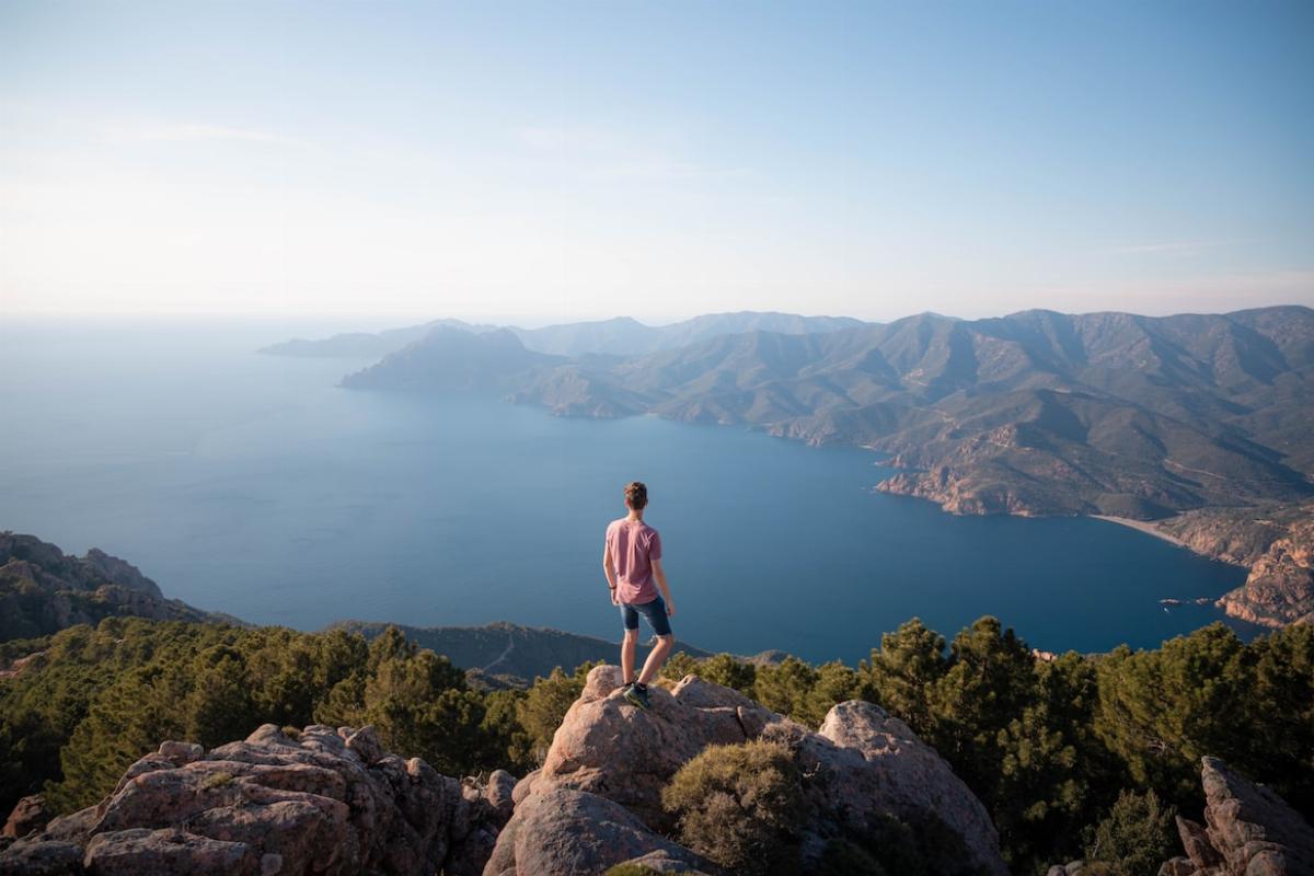 Un homme debout sur un rocher en haut d'une colline surplombant la mer en Corse